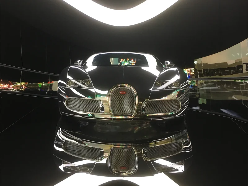 Frontansicht eines schwarzen Bugatti Veyron mit starken Lichtreflexionen in einer modernen Ausstellungshalle.